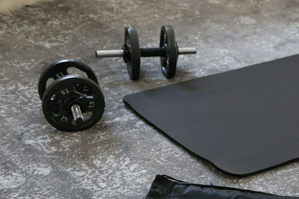 Two dumbbells beside a training mat in a sunlit room.
